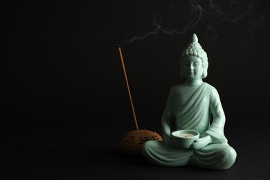 Photo of Beautiful ceramic Buddha sculpture with burning candle and incense stick on black background. Space for text
