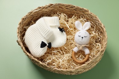 Different baby accessories in wicker box on green background, above view