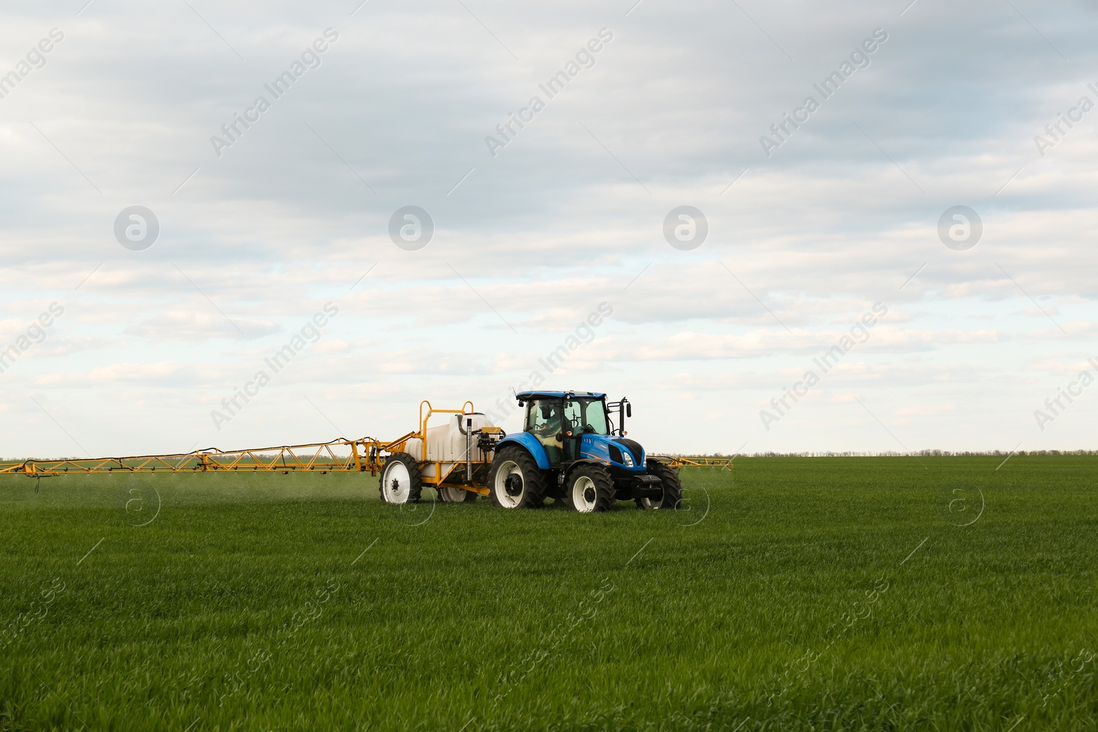 Photo of Tractor spraying pesticide in field on spring day. Agricultural industry