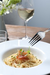Photo of Eating tasty spaghetti with prosciutto and microgreens at table, closeup. Exquisite presentation of pasta dish