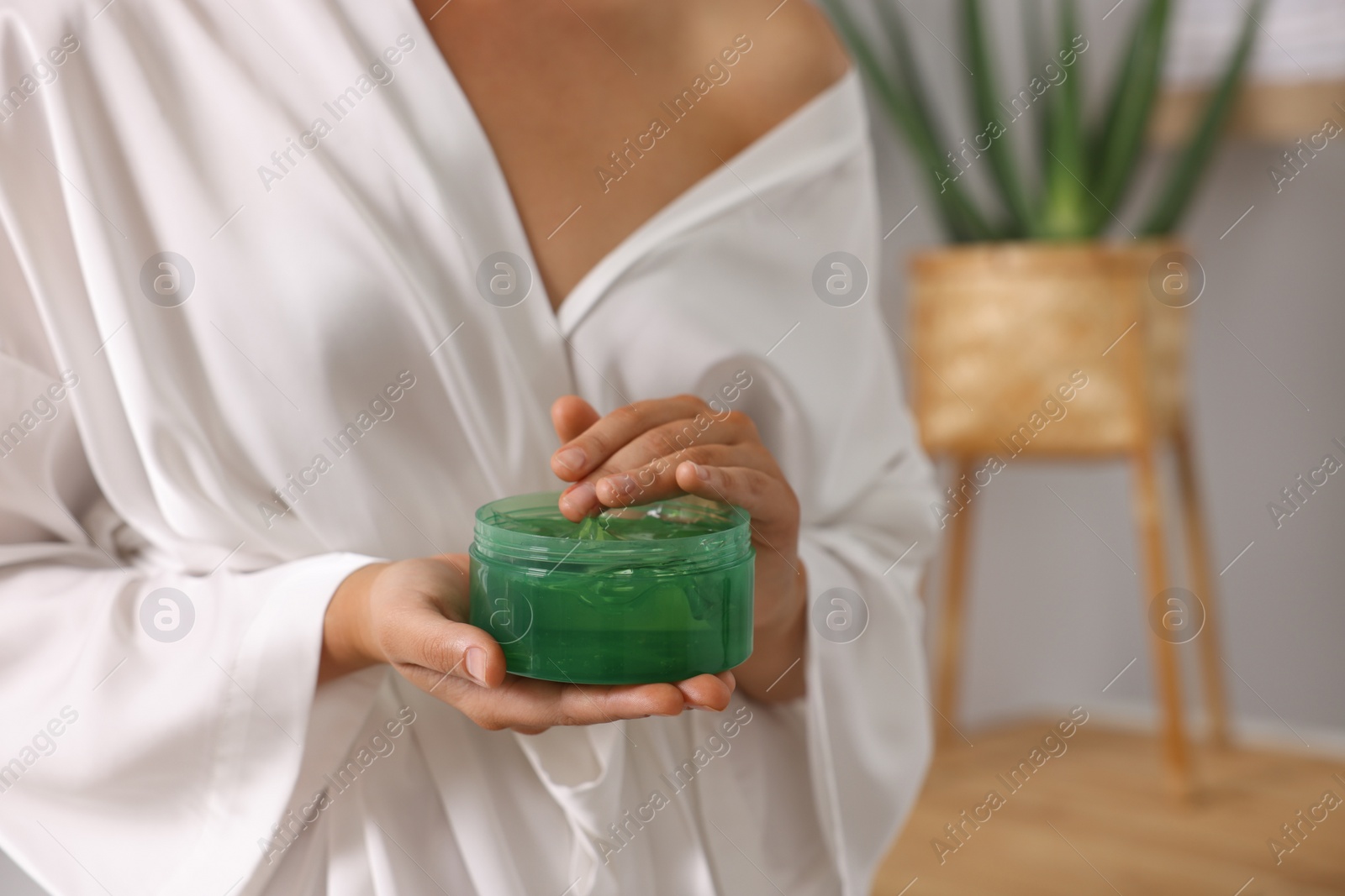 Photo of Young woman holding jar of aloe gel indoors, closeup. Space for text