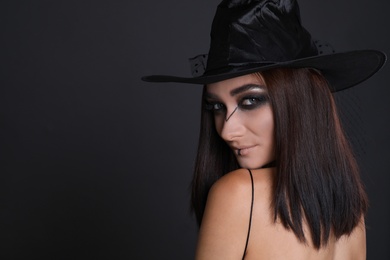 Mysterious witch wearing hat on black background, space for text