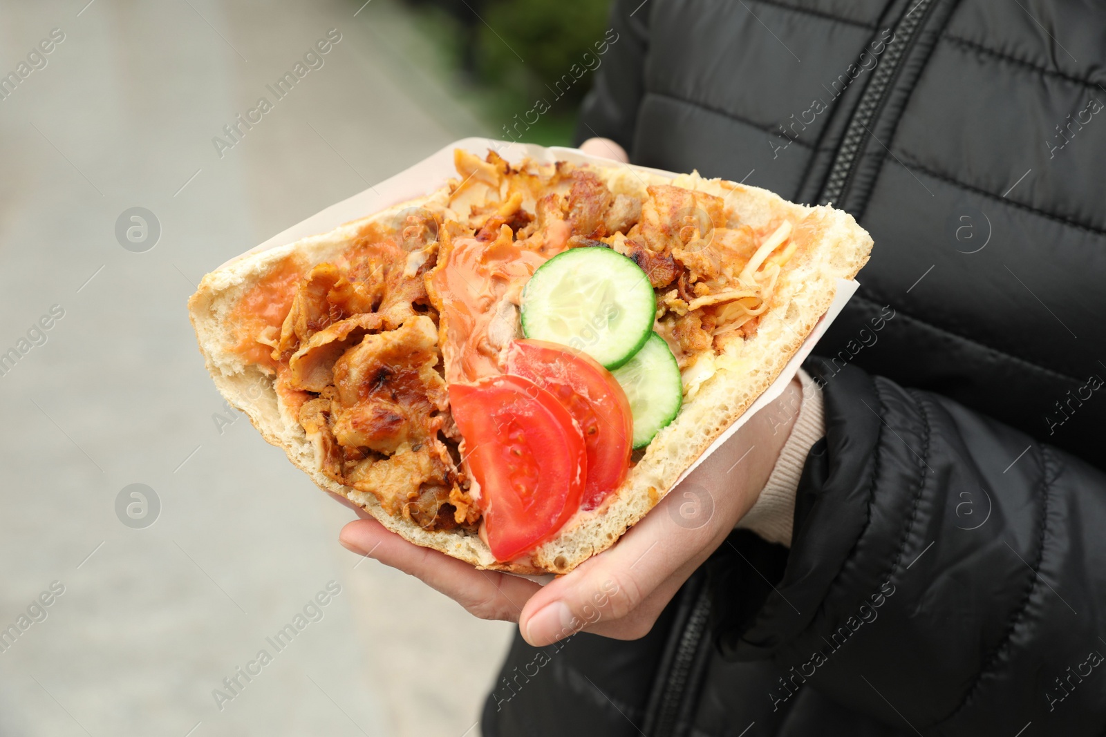 Photo of Woman holding delicious bread with roasted meat and vegetables outdoors, closeup. Street food