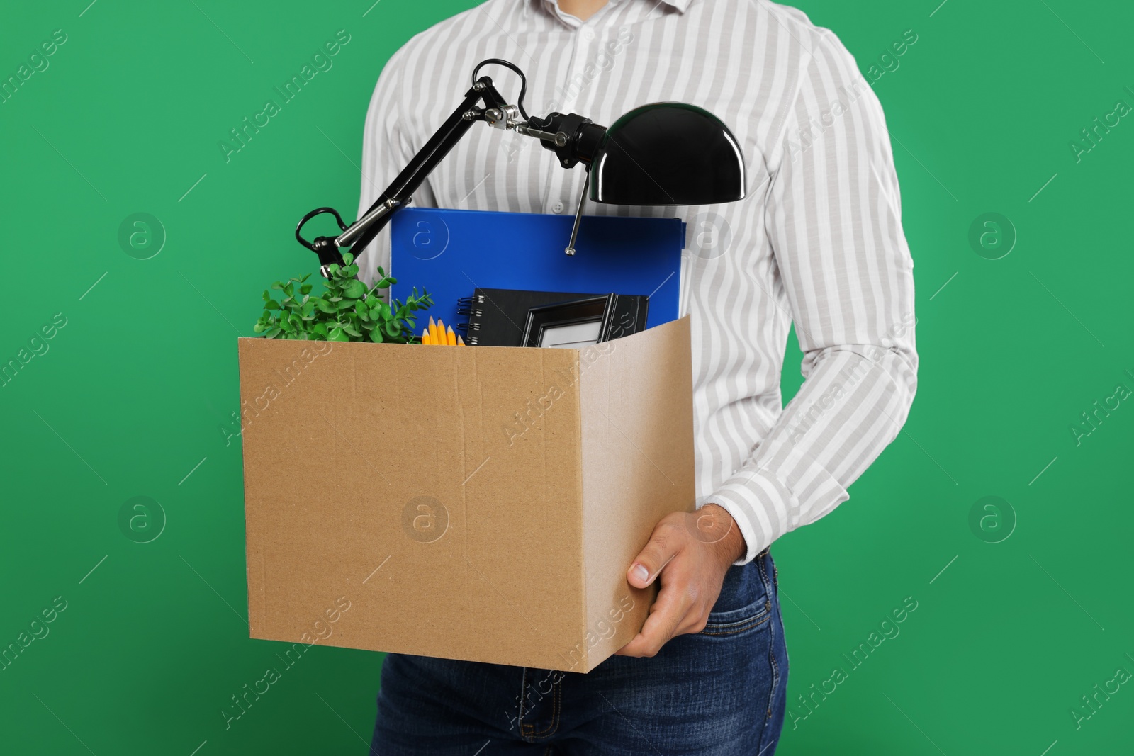 Photo of Unemployed man with box of personal office belongings on green background, closeup