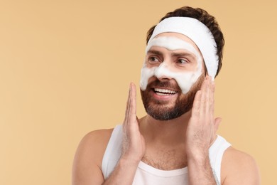 Photo of Man with headband washing his face on beige background, space for text