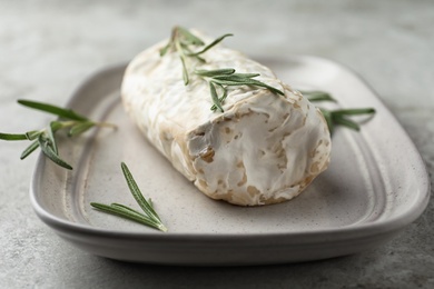 Delicious fresh goat cheese with rosemary on light grey table, closeup