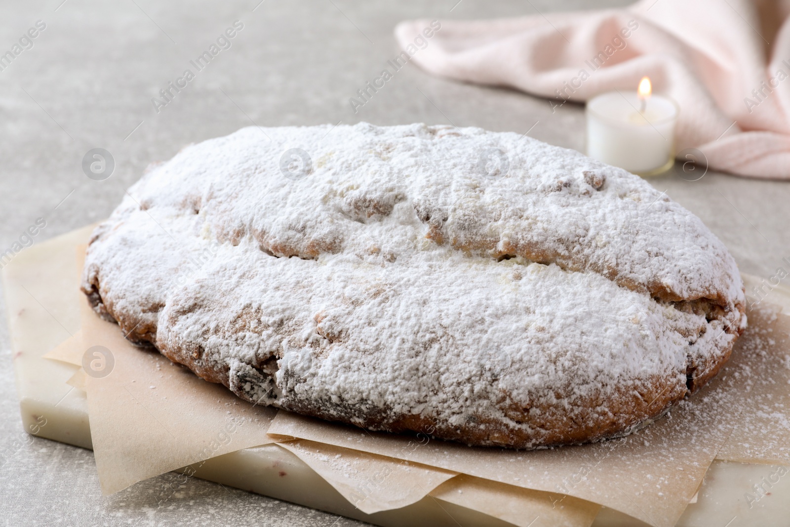 Photo of Delicious Stollen sprinkled with powdered sugar on light table, closeup