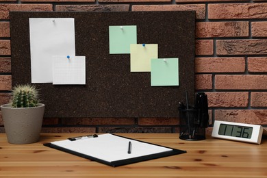 Photo of Corkboard with pinned notes hanging on brick wall over desk in office