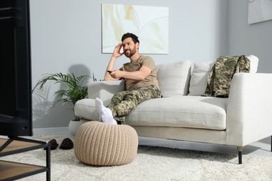 Photo of Happy soldier watching TV on sofa in living room. Military service