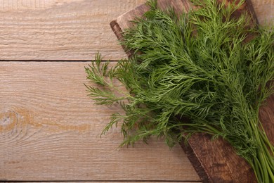 Photo of Board with sprigs of fresh dill on wooden table, top view. Space for text