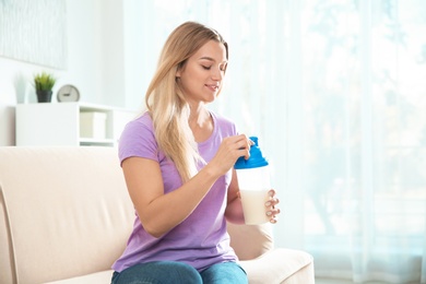 Photo of Young woman with bottle of protein shake sitting on sofa at home