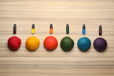 Photo of Colorful dough and bottles with food colorings on wooden table, flat lay