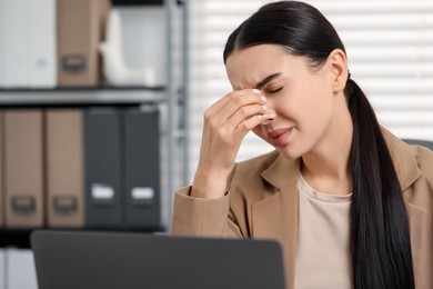 Woman suffering from headache at workplace in office, space for text