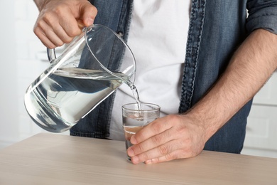 Man pouring water into glass at table, closeup