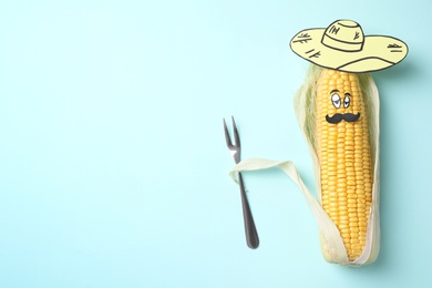 Photo of Mexican man of corncob, paper hat and fork on light blue background, top view. Space for text