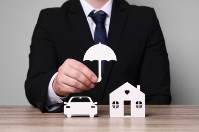 Photo of Man holding figure of umbrella above wooden table. closeup. Insurance concept