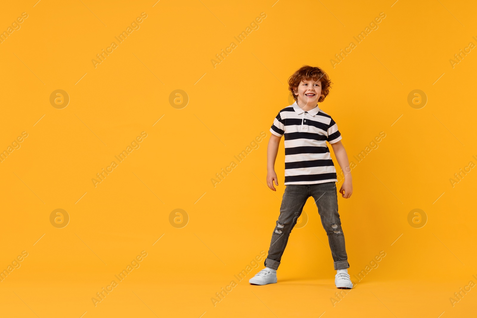 Photo of Happy little boy dancing on yellow background. Space for text