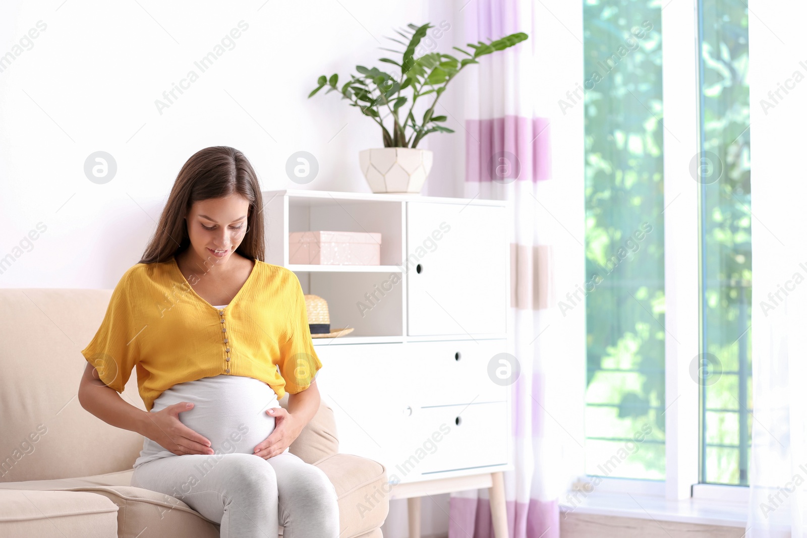 Photo of Pregnant woman sitting on sofa at home