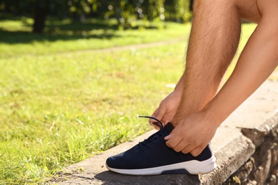 Sporty man tying shoelaces before running outdoors on sunny morning