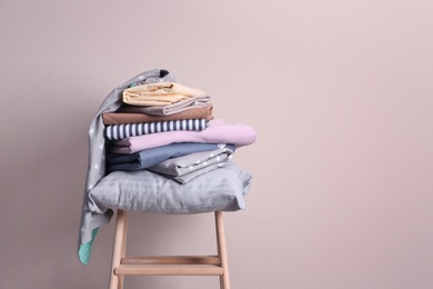 Photo of Stack of clean bed sheets and pillow on stool near beige wall. Space for text