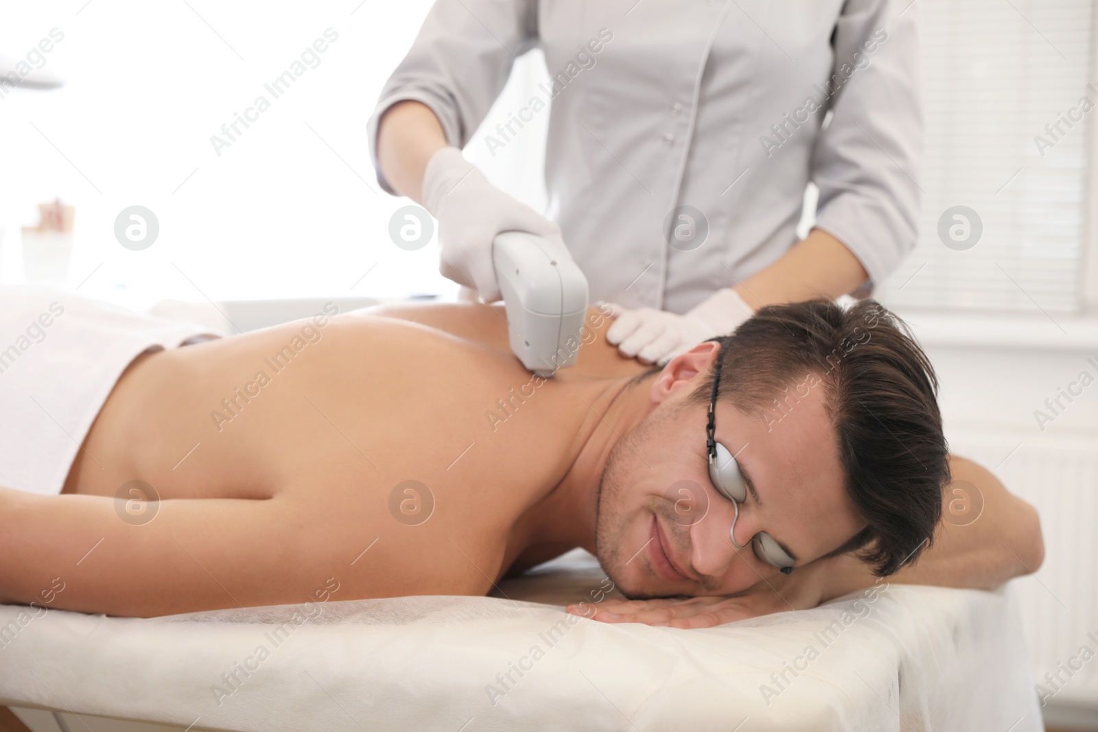 Photo of Young man undergoing laser epilation procedure in beauty salon