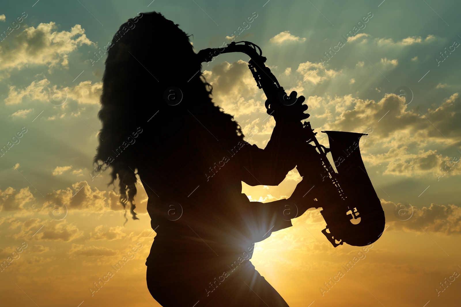 Image of Silhouette of woman playing saxophone against beautiful sky at sunset