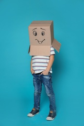 Photo of Cute little child wearing cardboard box with smiling face on color background