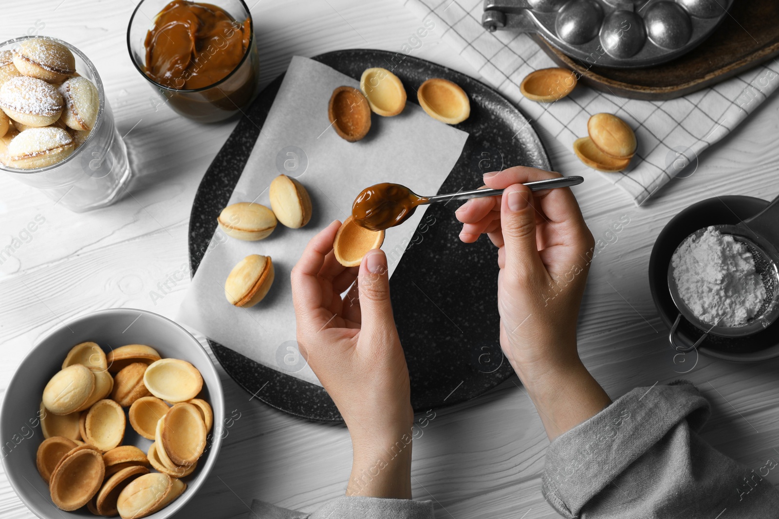 Photo of Woman making delicious walnut shaped cookies at white wooden table, above view