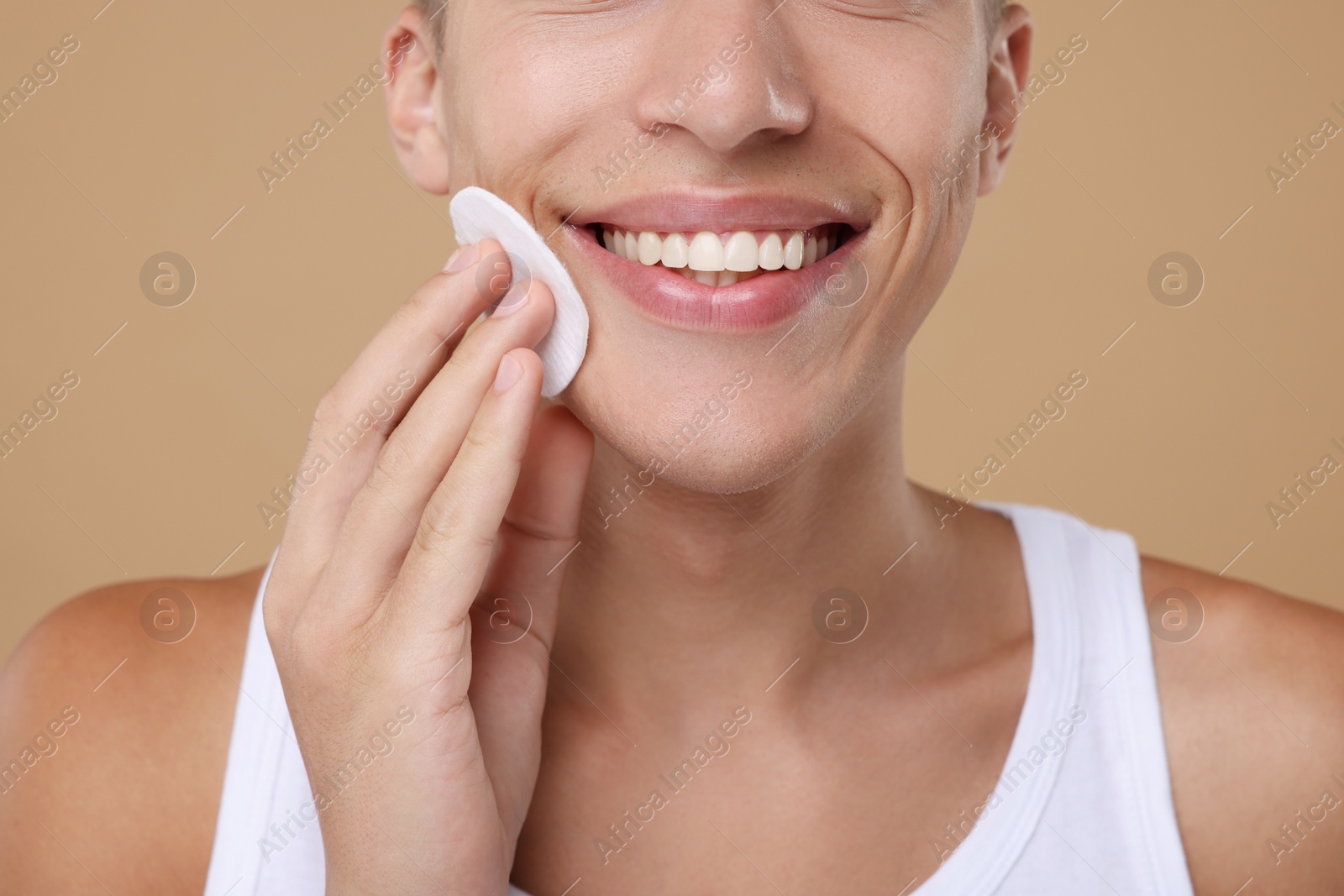 Photo of Man cleaning face with cotton pad on beige background, closeup