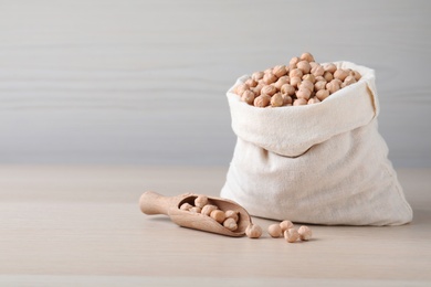 Photo of Sack and scoop with chickpeas on wooden table, space for text