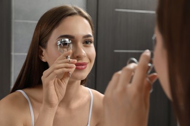 Woman using eyelash curler near mirror indoors