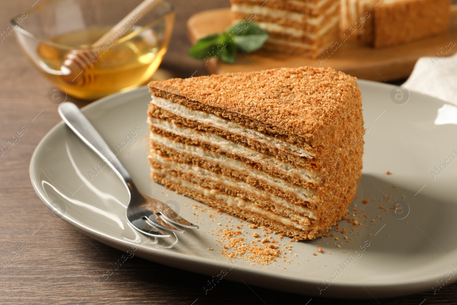 Photo of Slice of delicious layered honey cake served on wooden table, closeup