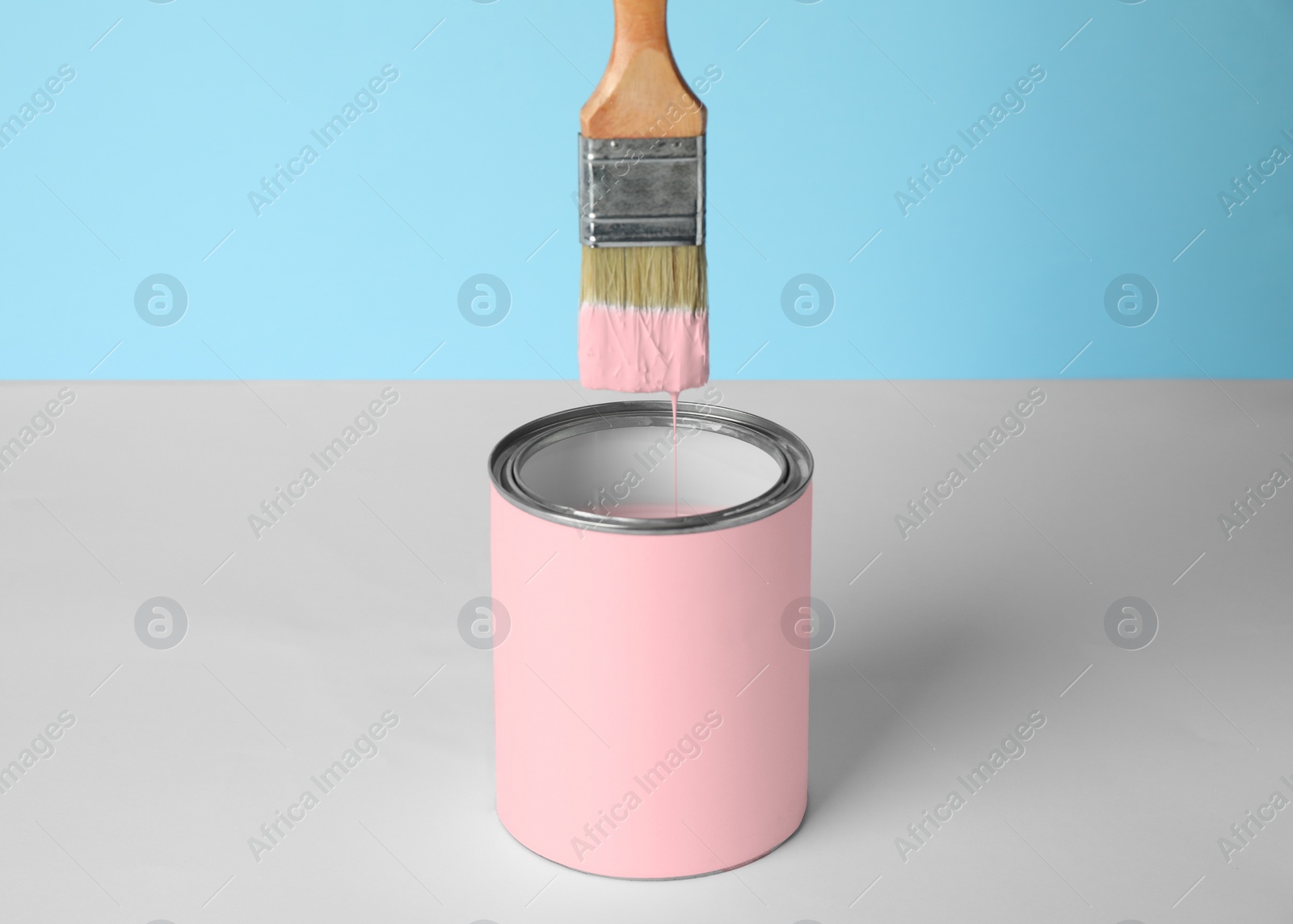 Photo of Brush over can of pink paint on table against blue background