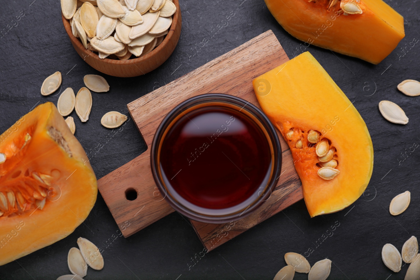 Photo of Flat lay composition with glass bowl of pumpkin seed oil on black table