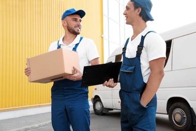 Photo of Male movers with box and clipboard near van outdoors