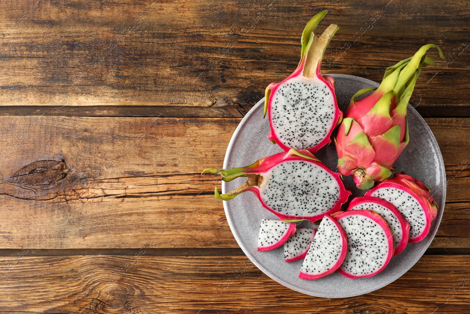 Photo of Delicious cut and whole dragon fruits (pitahaya) on wooden table, top view. Space for text