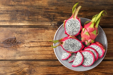 Photo of Delicious cut and whole dragon fruits (pitahaya) on wooden table, top view. Space for text