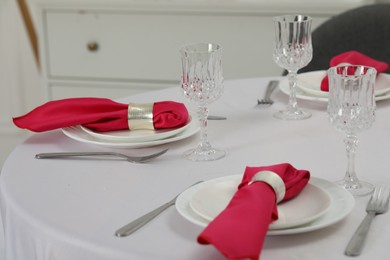 Color accent table setting. Glasses, plates, cutlery and pink napkins on table indoors