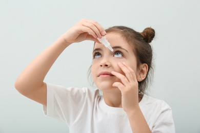 Photo of Adorable little girl using eye drops on white background