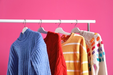 Collection of warm sweaters hanging on rack against color background