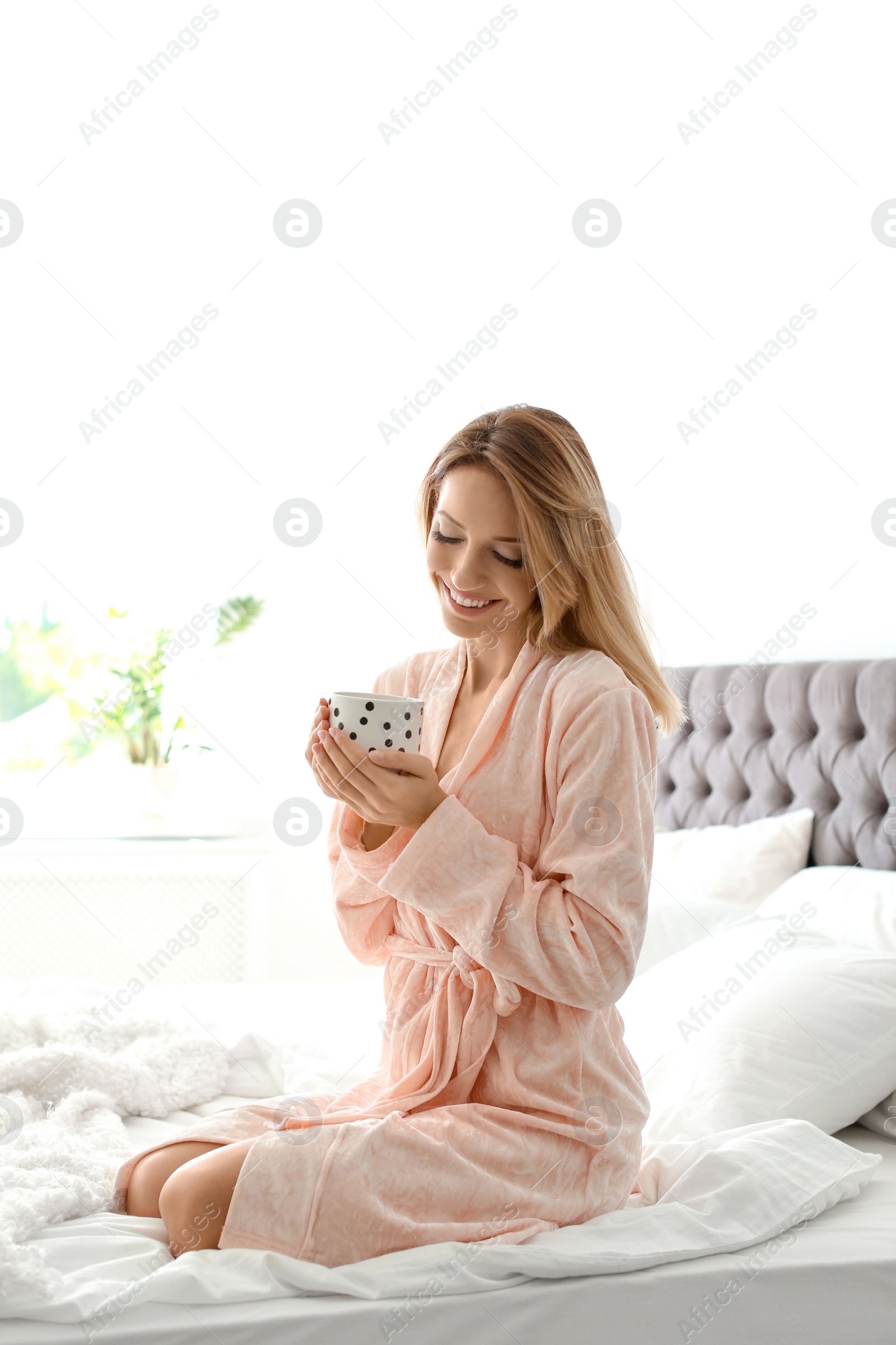 Photo of Beautiful young woman with cup of coffee sitting in bed at home. Lazy morning