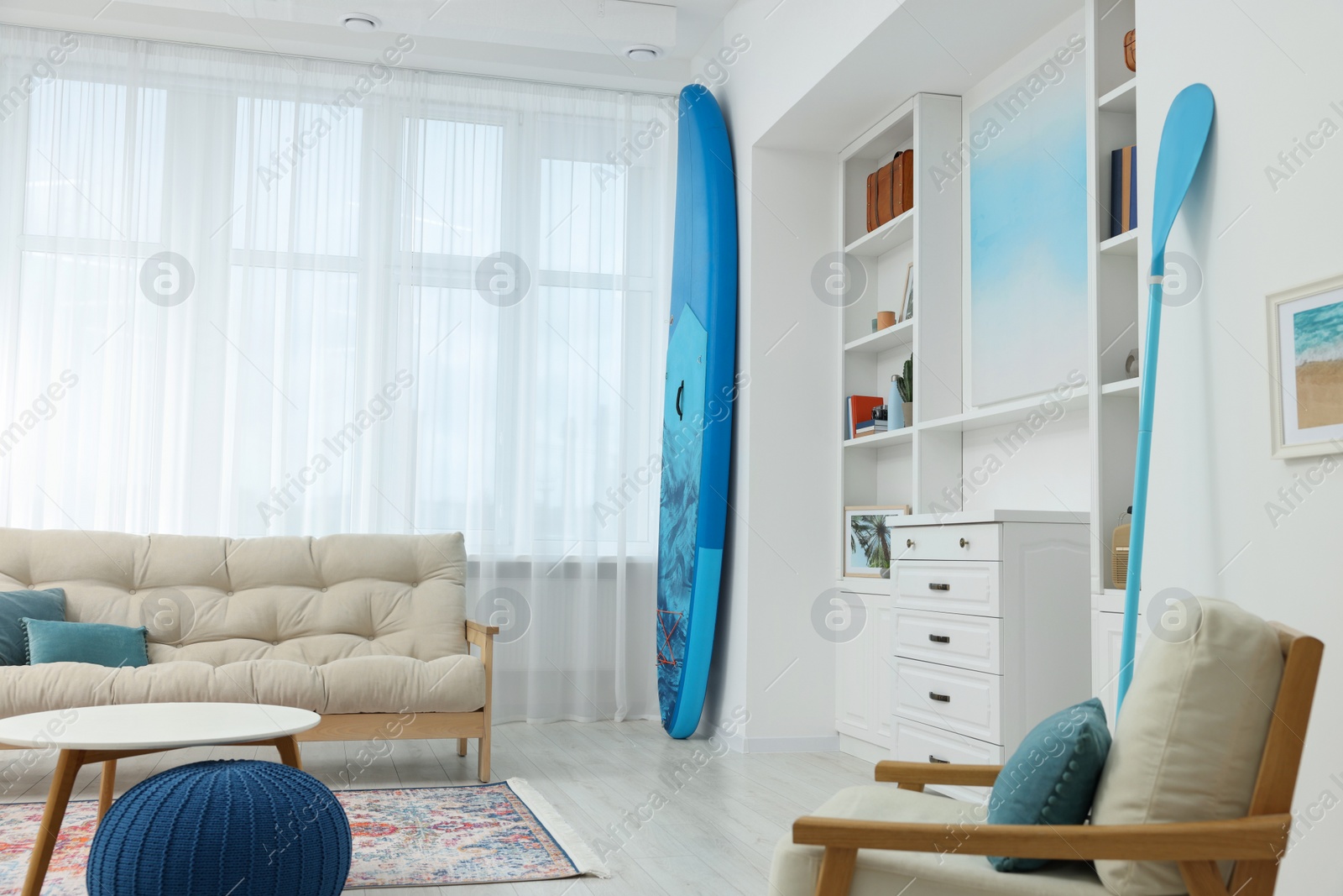 Photo of SUP board and modern furniture in stylish living room. Interior design