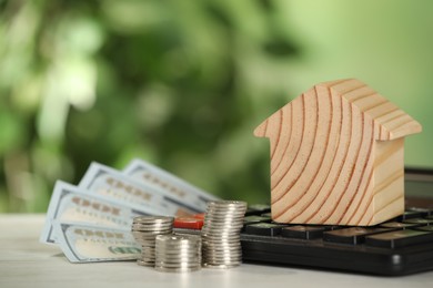 Photo of Mortgage concept. House model, money and calculator on white table against blurred background, space for text