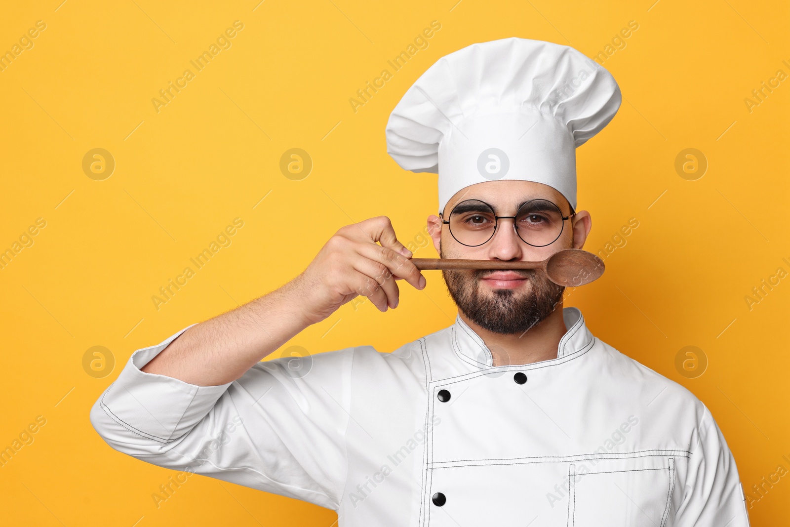 Photo of Professional chef with wooden spoon having fun on yellow background