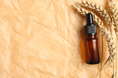 Photo of Bottle with organic cosmetic product and ears of wheat on parchment paper, flat lay. Space for text