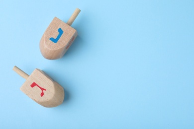 Photo of Hanukkah traditional dreidels with letters Nun and Gimel on light blue background, flat lay. Space for text