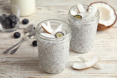 Photo of Tasty chia seed pudding with coconut in jars and ingredients on table