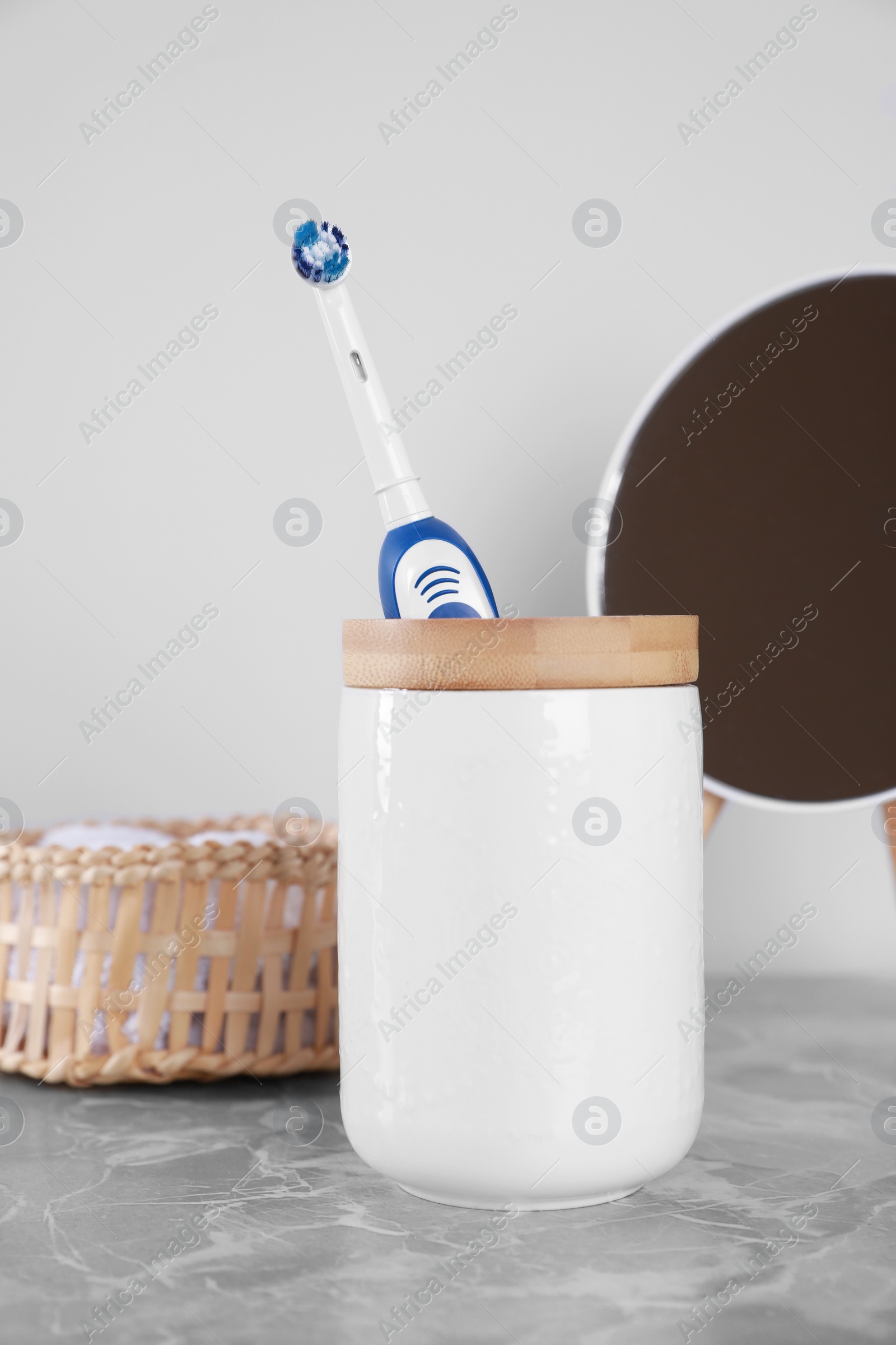 Photo of Electric toothbrush in holder, mirror and towel on light grey marble table near white wall