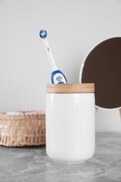 Photo of Electric toothbrush in holder, mirror and towel on light grey marble table near white wall
