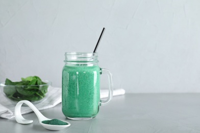 Photo of Spoon with spirulina powder and mason jar of smoothie on table against light background. Space for text